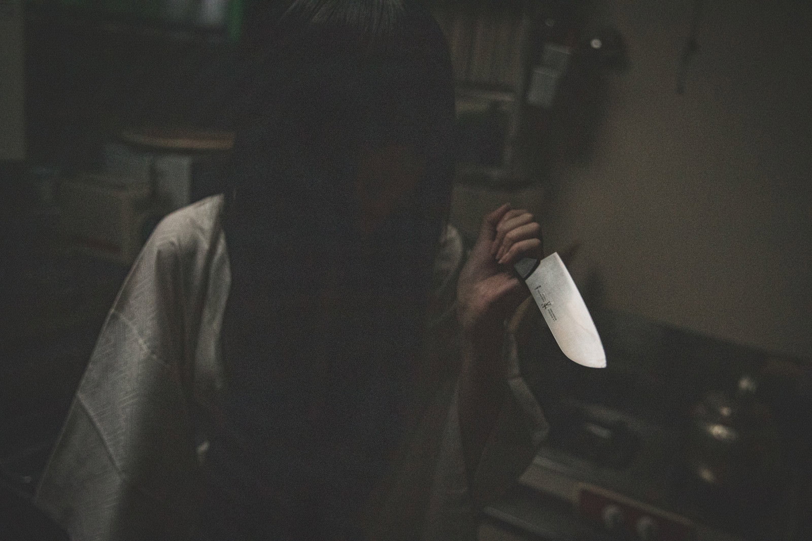薄暗い場所で包丁を持つ黒髪の女性のホラー写真［モデル：緋真煉］