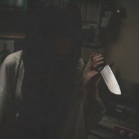 暗がりで包丁を握る黒髪の女性の怨霊の表情の写真