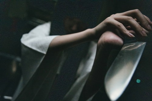 研ぎたての包丁を見せつけてくる白いシャツの手