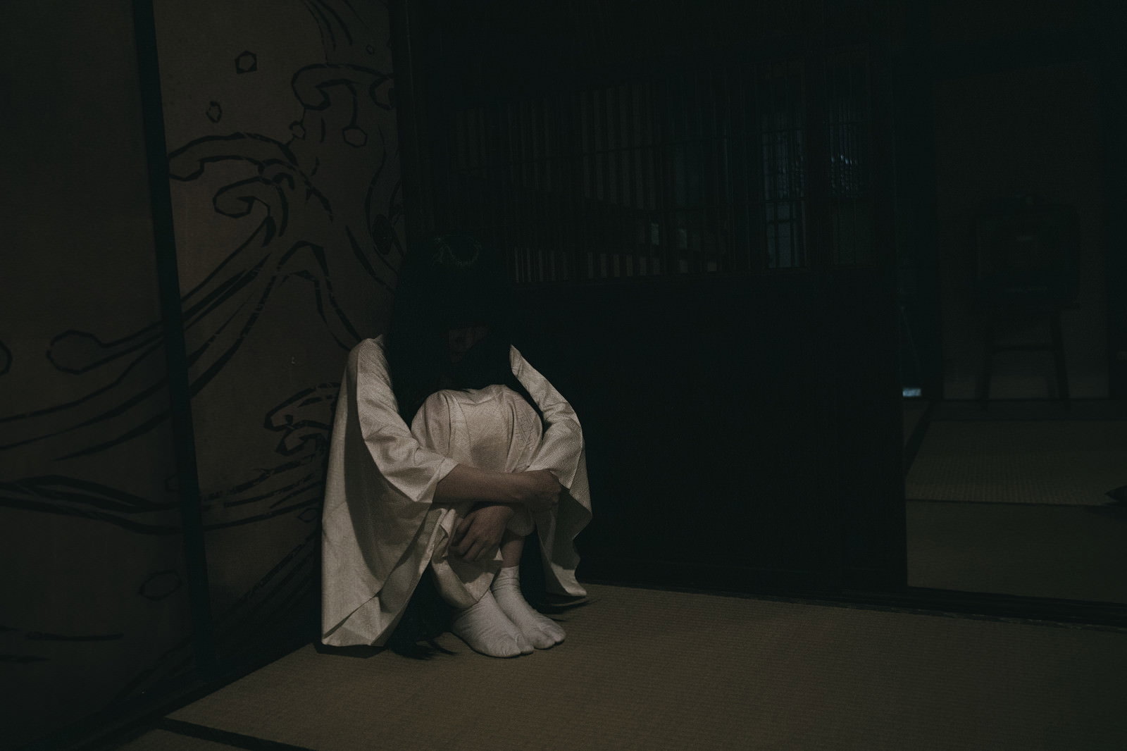 暗い部屋で体育座りする女性［モデル：緋真煉］