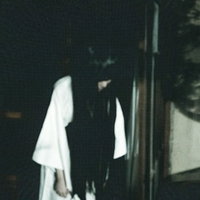 窓際で俯く白い服の女性、暗い室内で窓からの淡い光に照らされるの写真