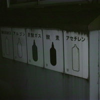 薄暗い倉庫に並ぶ酸素やアセチレンなどの危険物看板の写真