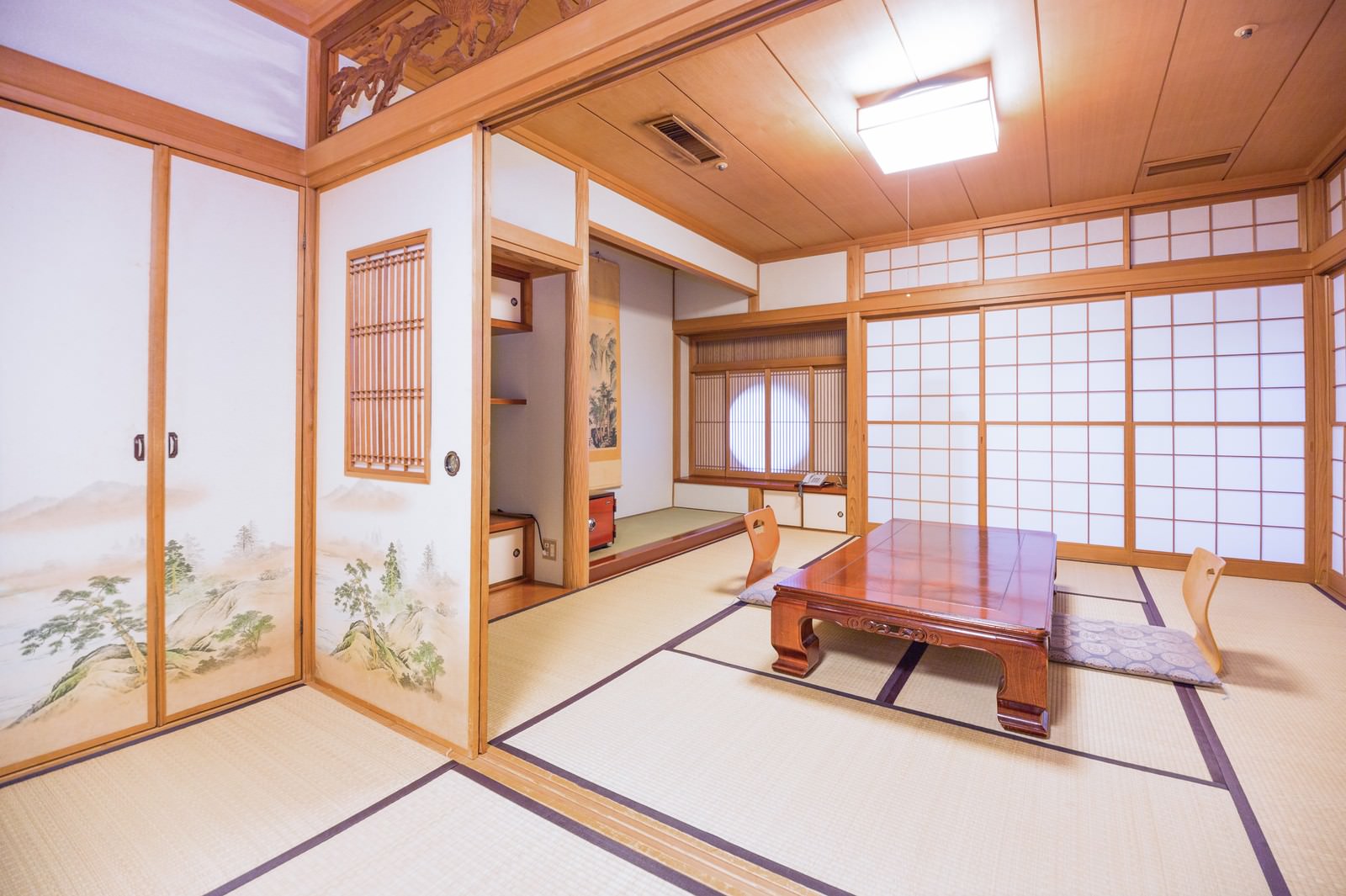 畳に座布団と低いテーブルが配置された木の梁と柱がある広い和室