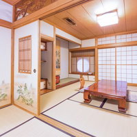 畳に座布団と低いテーブルが配置された木の梁と柱がある広い和室の写真