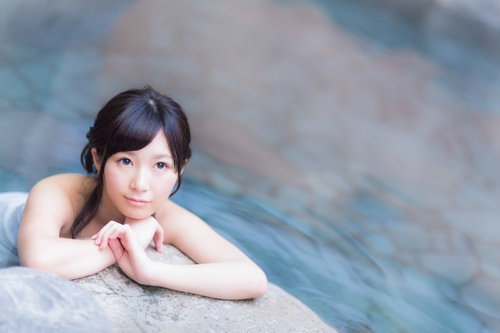 温泉の湯船の縁で寛ぐ女性、穏やかな表情で入浴