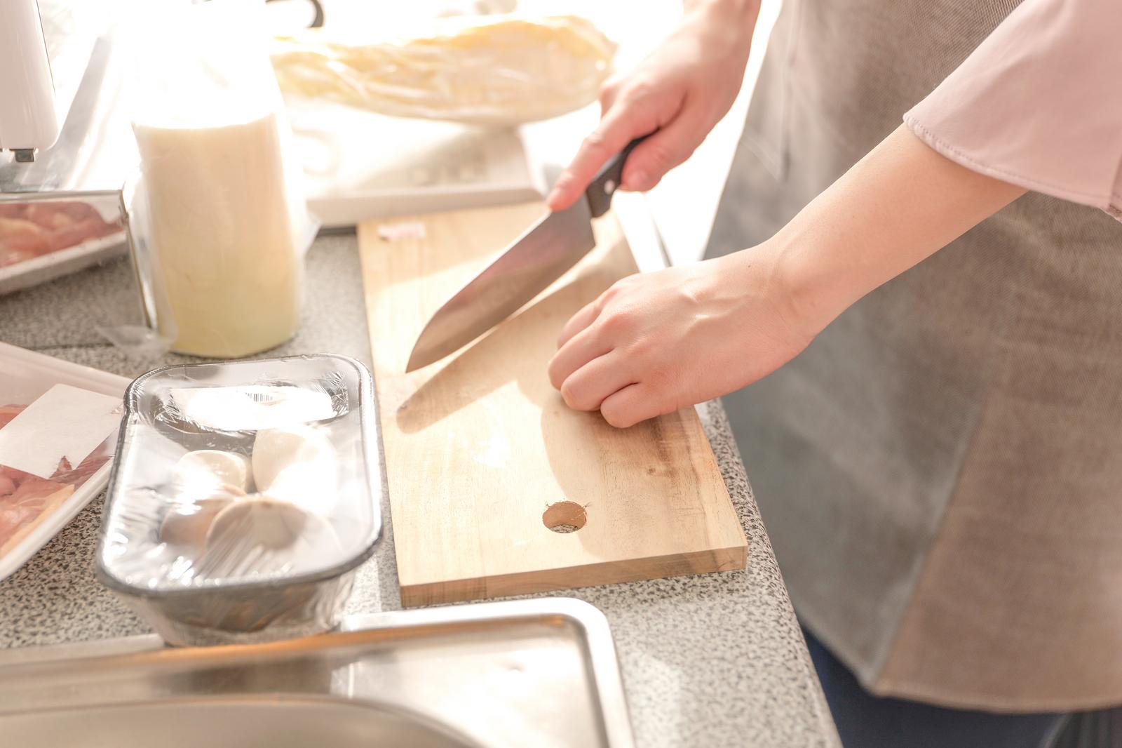 木のまな板で包丁を使い料理をする女性の手元