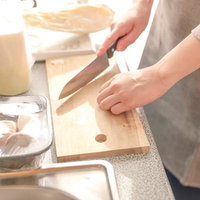 木のまな板で料理する家庭の台所、包丁で食材をカットする調理風景の写真