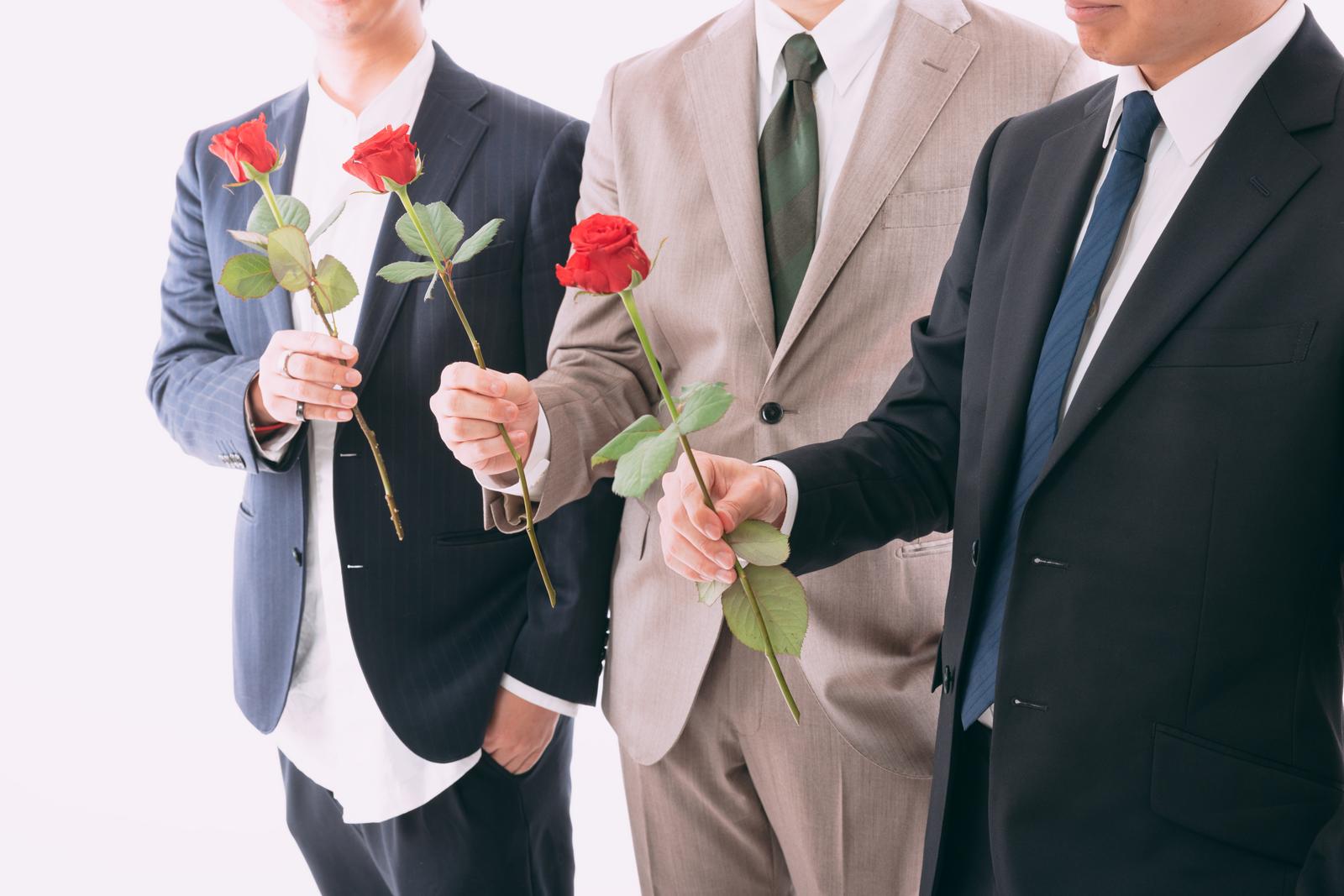 スーツ姿の男性3人が赤いバラを手に持ち並んでいる