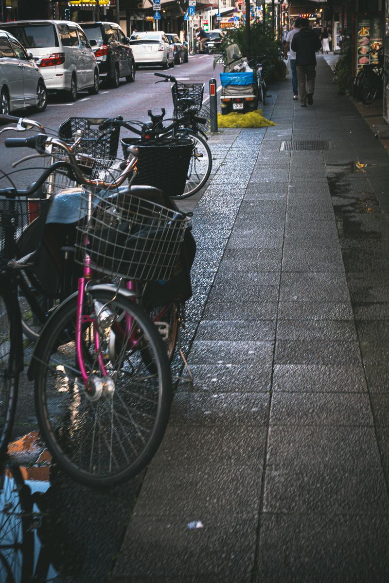 福富町商店街の歩道に駐輪されたカゴ付き自転車と奥に見える商店や自動車