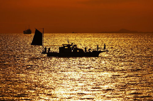 夕焼け色に染まる海面に浮かぶ漁船のシルエット