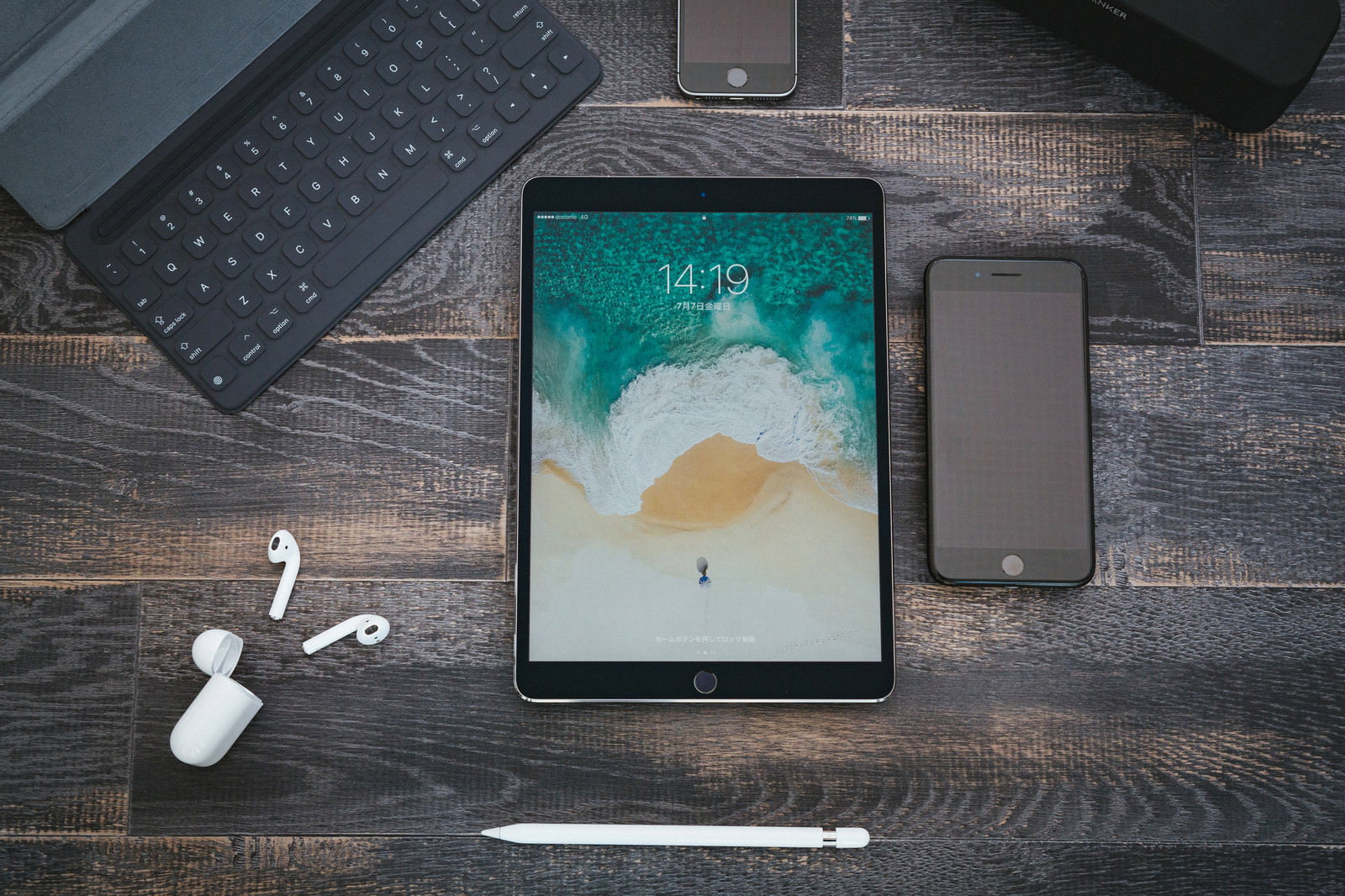 木目調の床に置かれたスマートフォン、タブレット、イヤホン、ペンシル