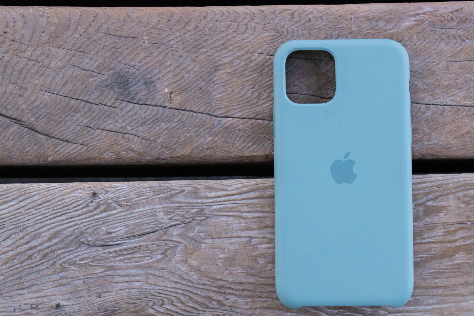 木目のウッドデッキの上に置かれたブルーのiPhone 11 Pro純正シリコンケース