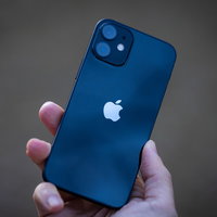 うっすらと空が映り込むiPhone12の背面を持つ手の写真