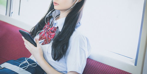 通学中にスマホで音楽を聴く女子高生、有線イヤホン姿