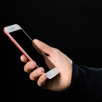 黒い背景で白いスマートフォンを握る手の操作風景の写真