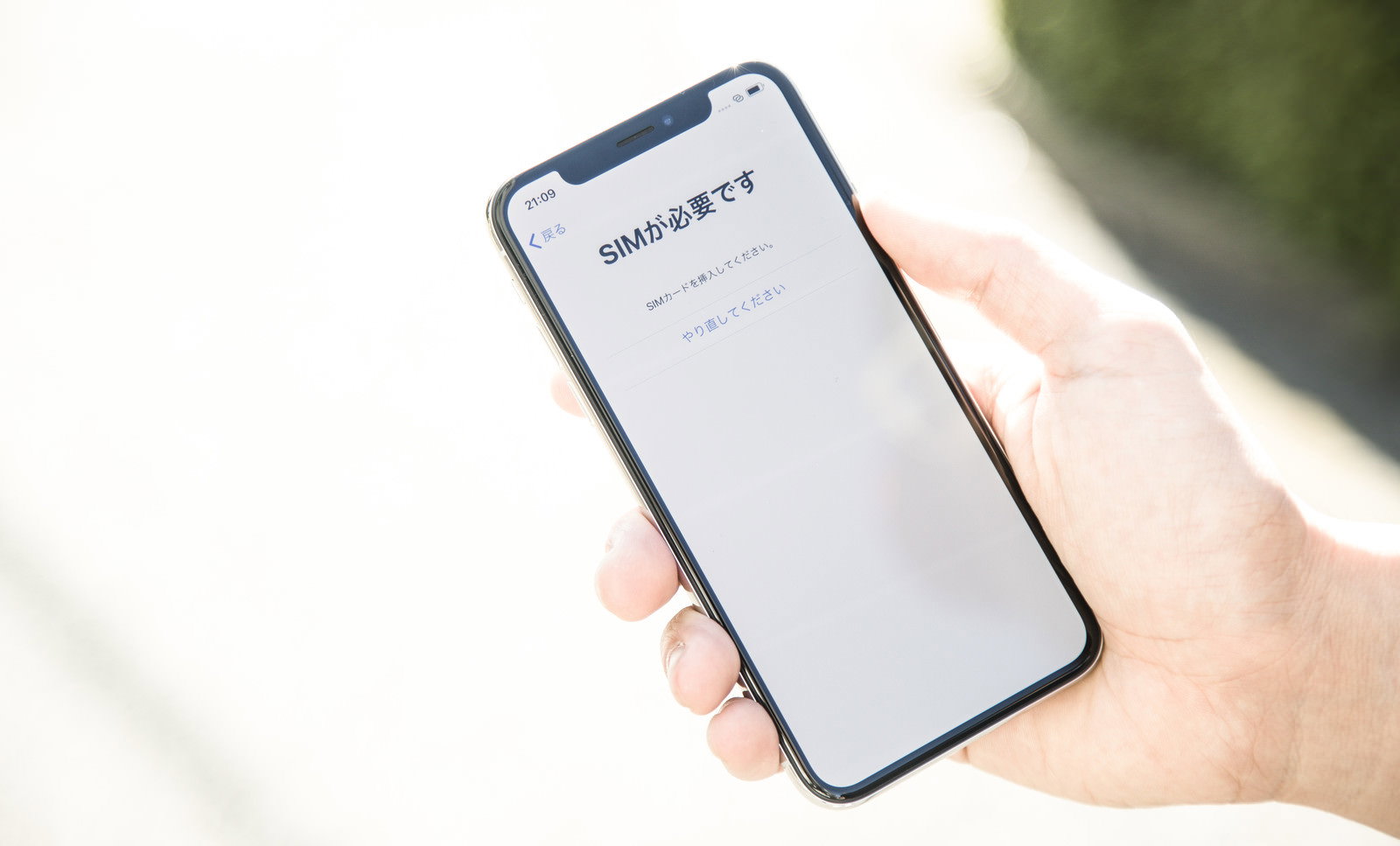 スマートフォンのSIM挿入画面を表示したiPhoneXを持つ手