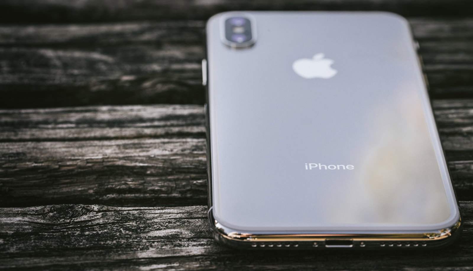 木目調の机の上に置かれたiPhone Xの背面とAppleロゴ