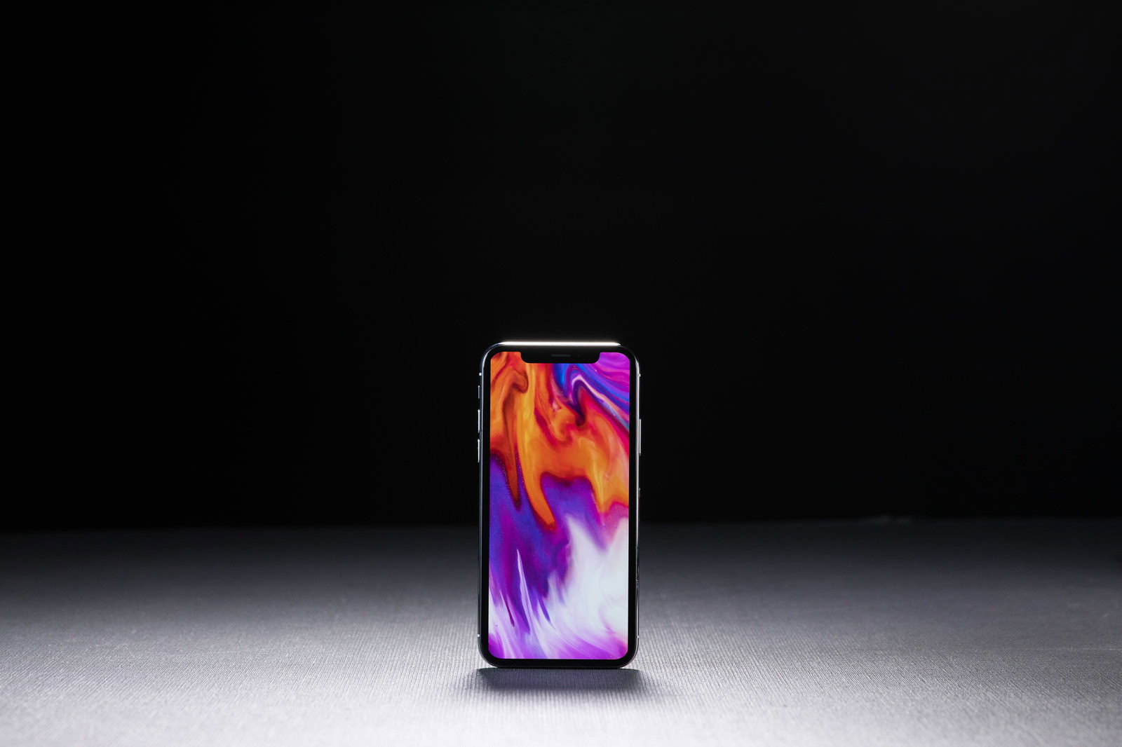 暗いグラデーション背景の上に置かれたiPhone X
