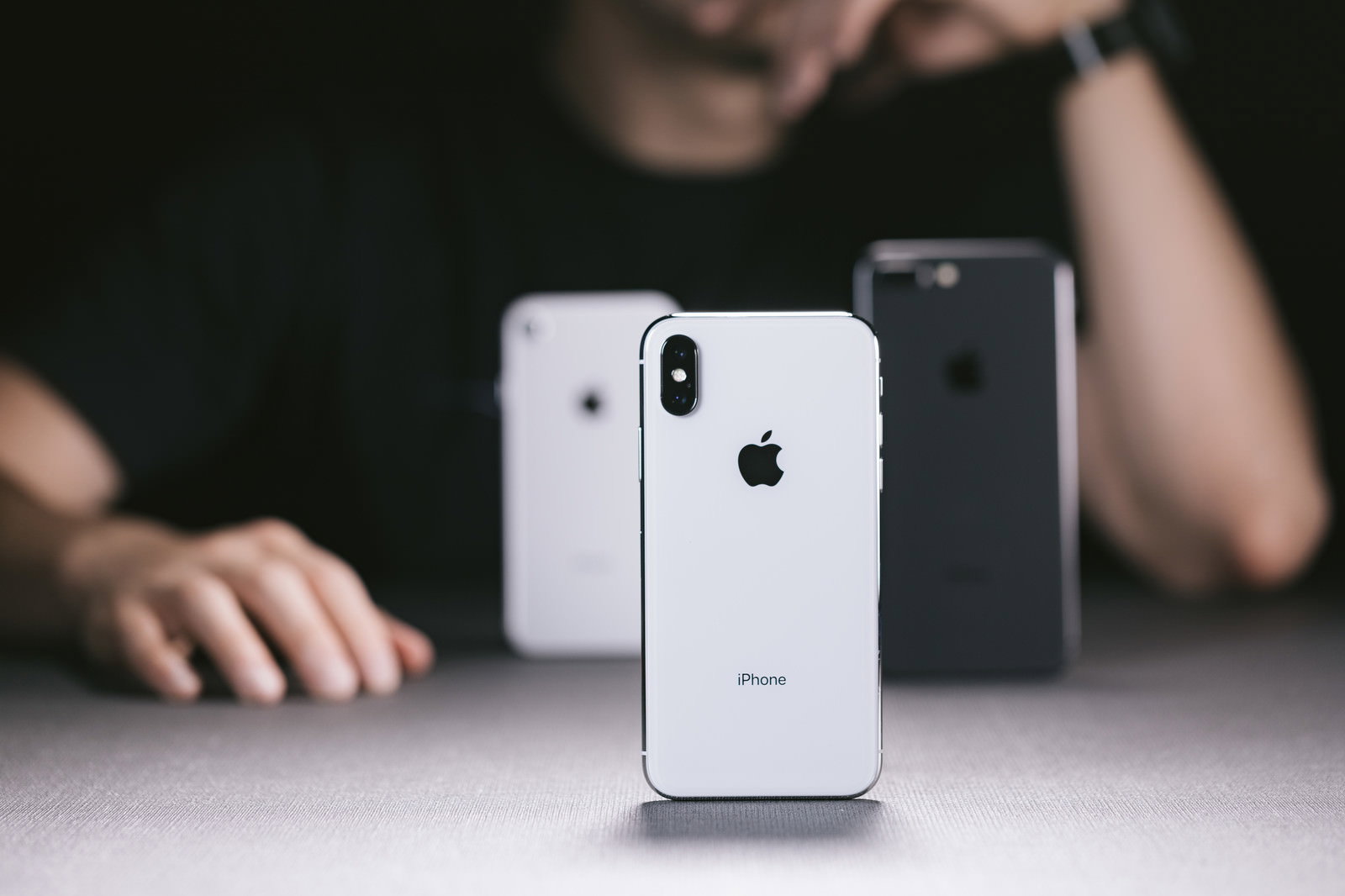 白いデスクに置かれたiPhone XとiPhone 8を見て考える男性