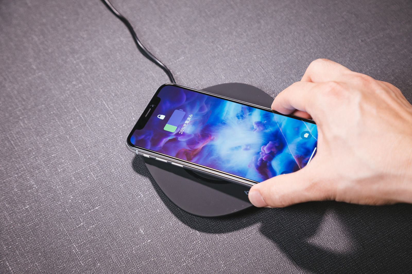 ワイヤレス充電器の上でスマートフォンを充電している手元
