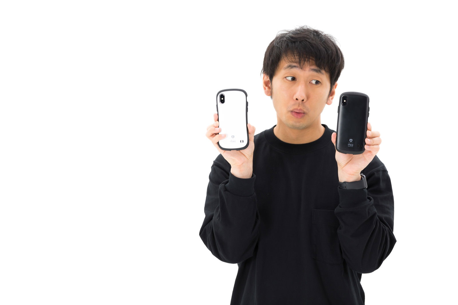 白いスマホと黒いスマホを両手に持ち迷っている男性［モデル：大川竜弥］