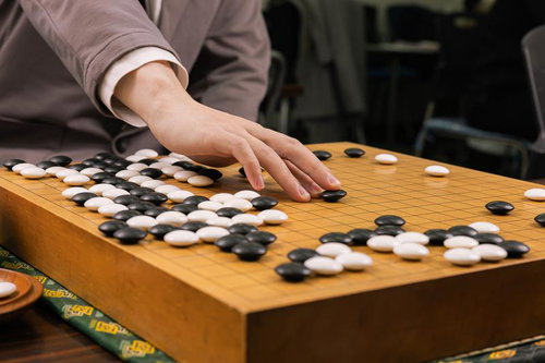 囲碁の対局で耳赤の一手を打つ手元の瞬間、木製碁盤での真剣な戦局