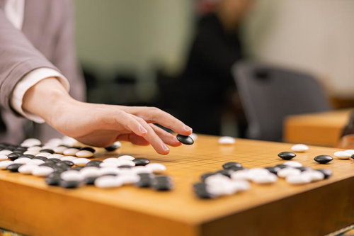碁盤に向かう手が打つ黒石（耳赤の一手）木製碁盤での対局場面