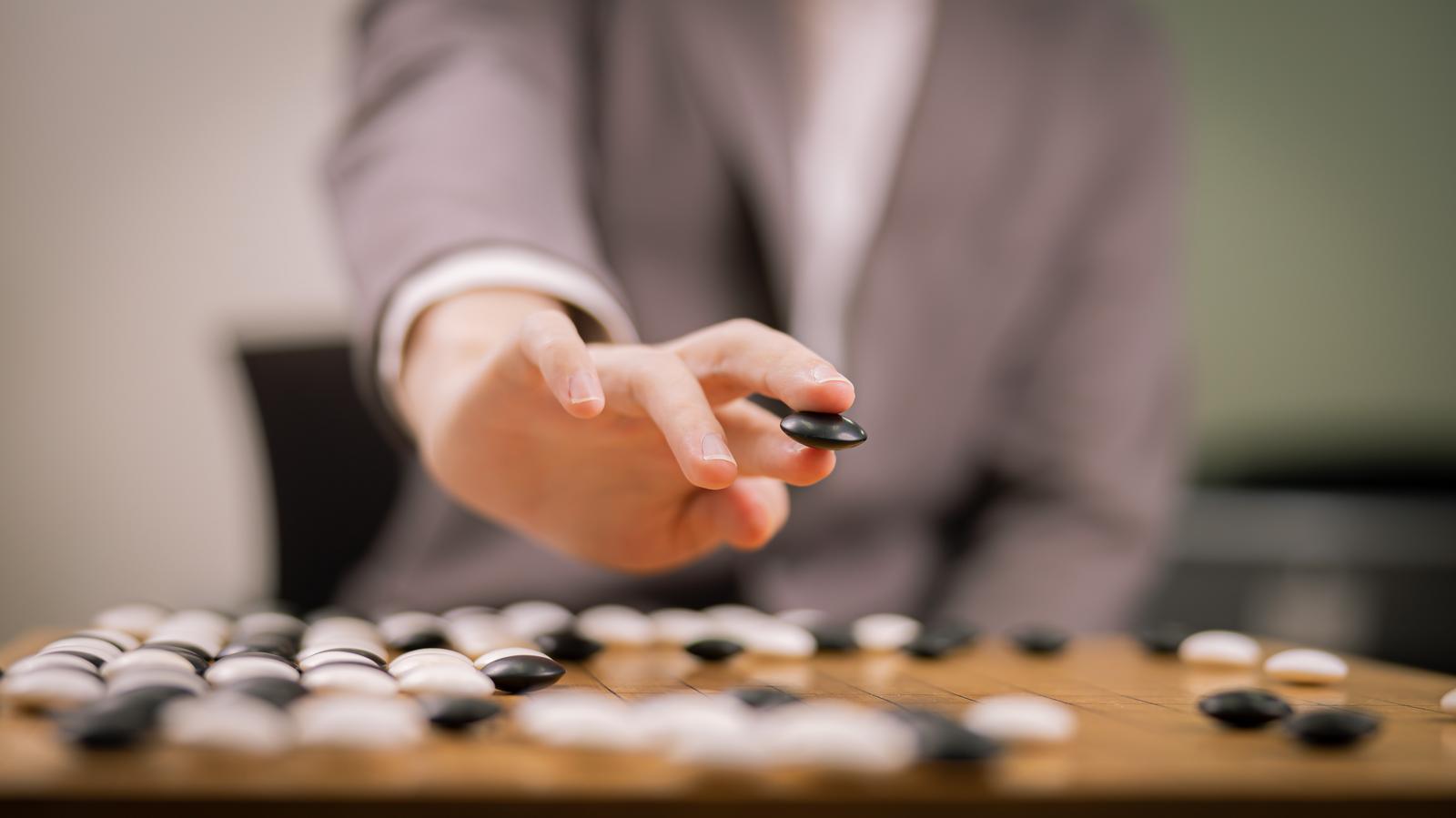 黒い碁石を持つ手元で、碁盤上に一手を打つプロ棋士
