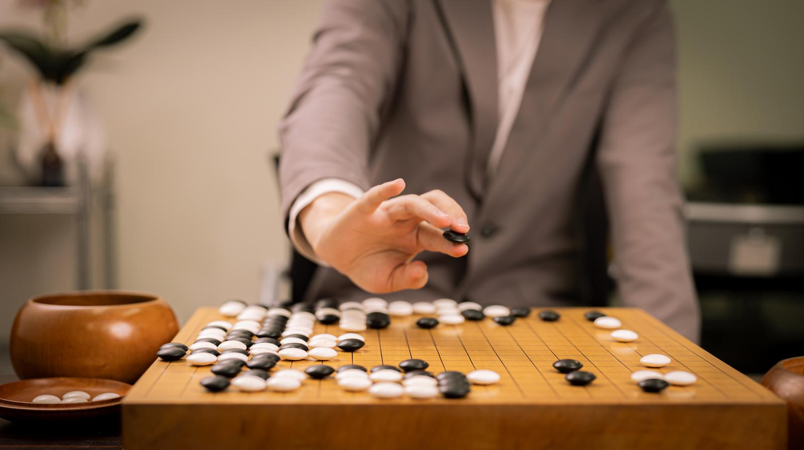 囲碁の碁盤で黒石を打つプロ棋士の手元、本因坊秀策の赤耳の一手を再現