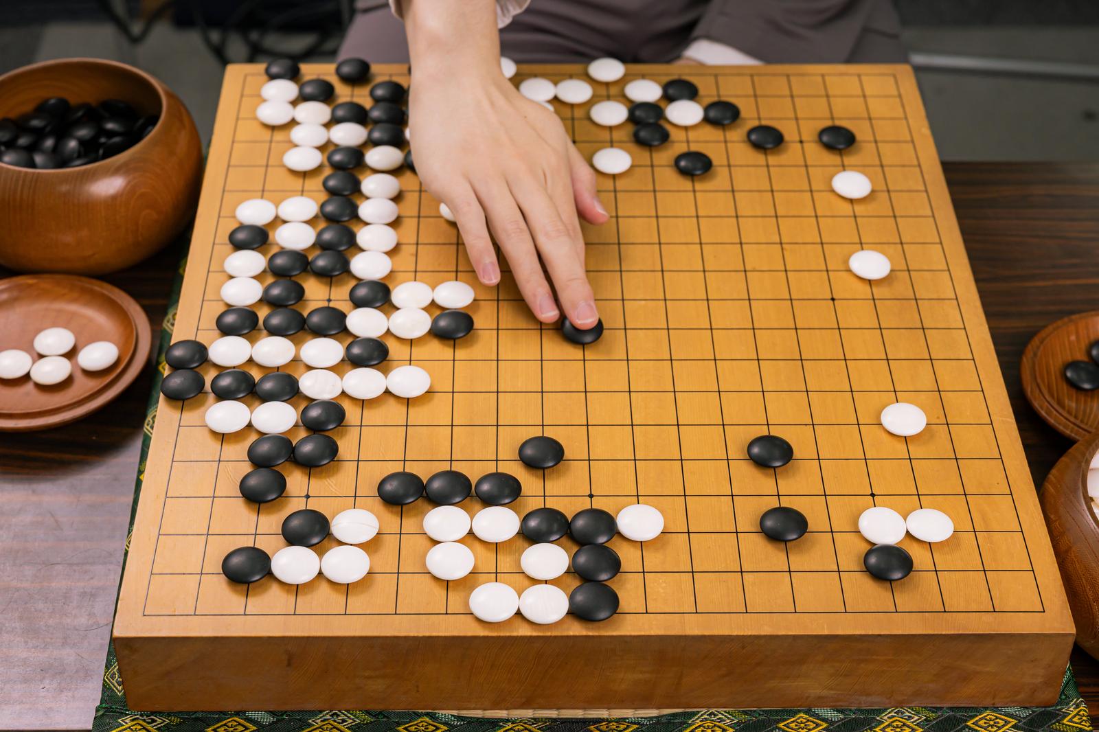 碁盤の上に黒白の碁石が並び、プレイヤーが石を打とうとしている囲碁の対局シーン