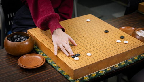 女性にも人気の囲碁。赤い袖をした女性が碁盤に黒石を置く対局風景