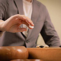 碁笥から取り出した碁石を碁盤に打つ前の瞬間、二本の指で持っている状態の写真