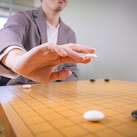 白石を二本の指で持ち碁盤に向かう瞬間の対局風景の写真