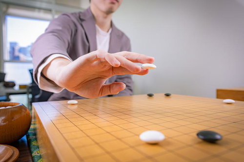 白石を二本の指で持ち碁盤に向かう瞬間の対局風景