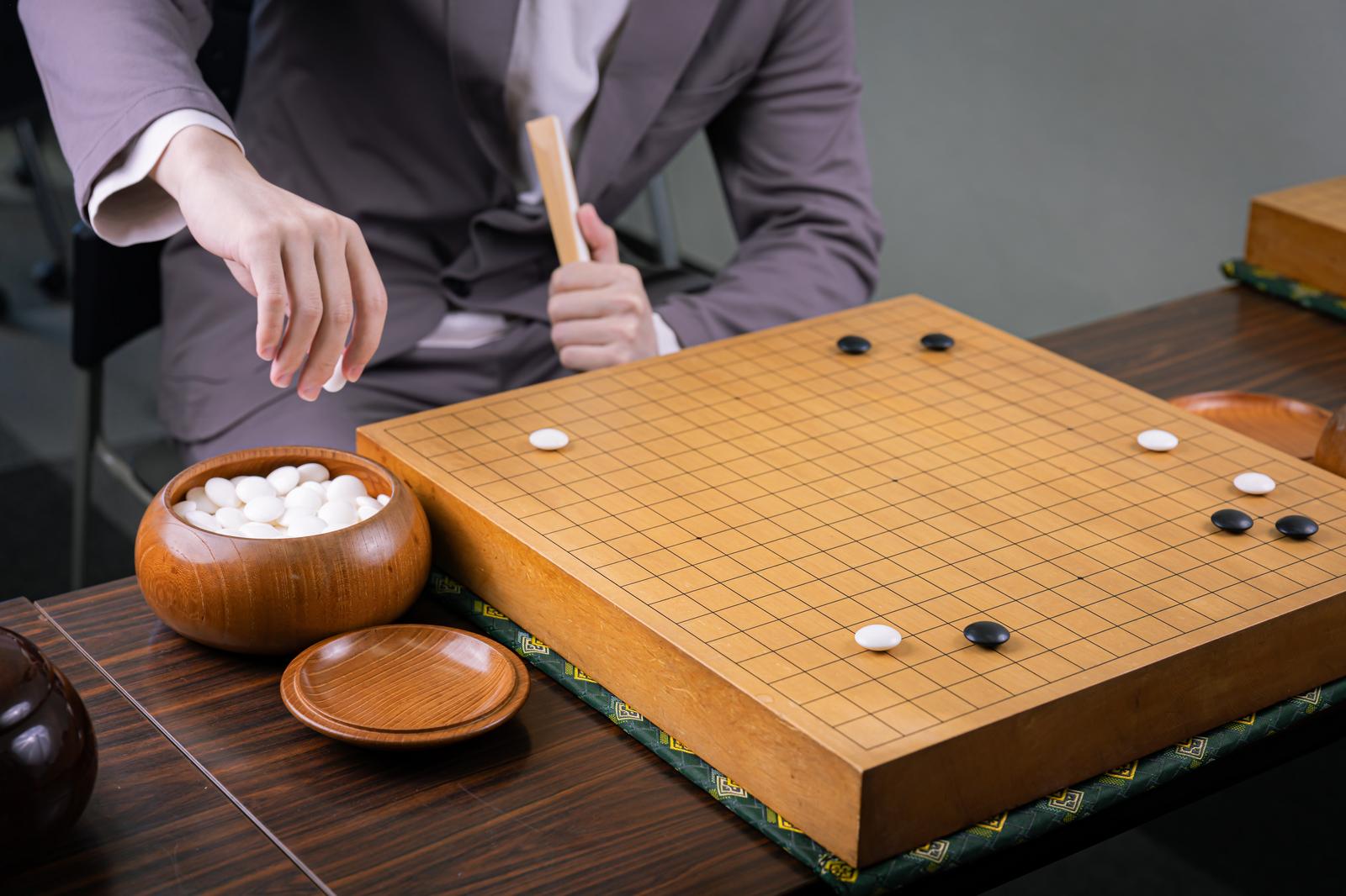 囲碁の対局で白石を打つプロ棋士、木製の碁盤と碁石
