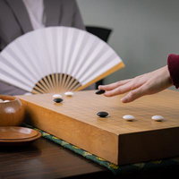 白と黒の碁石が並ぶ碁盤の前で扇子を持つ囲碁棋士の対局風景の写真
