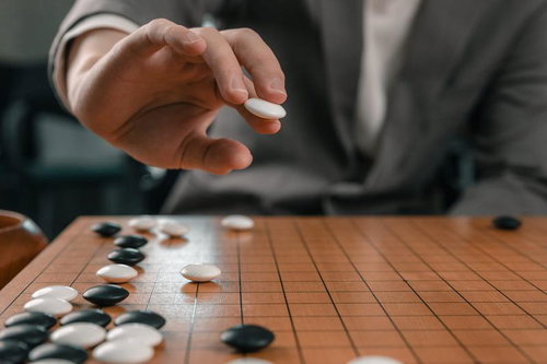 次の一手へ向かう溜めの静謐な瞬間、白い碁石を打つ手