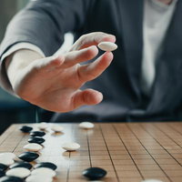 碁石を打ち下ろす一手の反動、紺色スーツの男性の手の写真