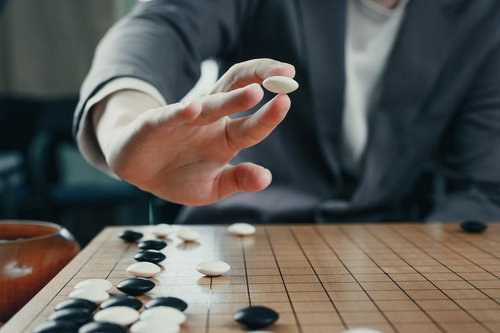 碁石を打ち下ろす一手の反動、紺色スーツの男性の手