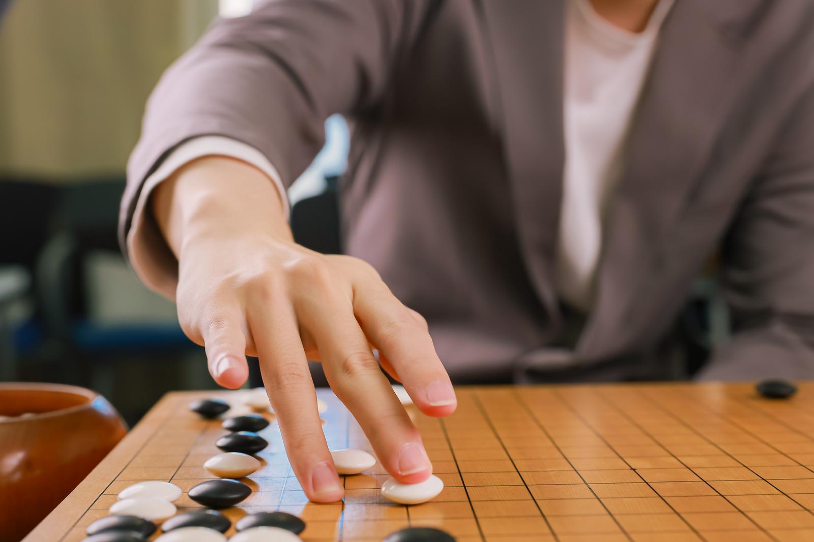 棋士が囲碁盤に白石を打つ瞬間の手元