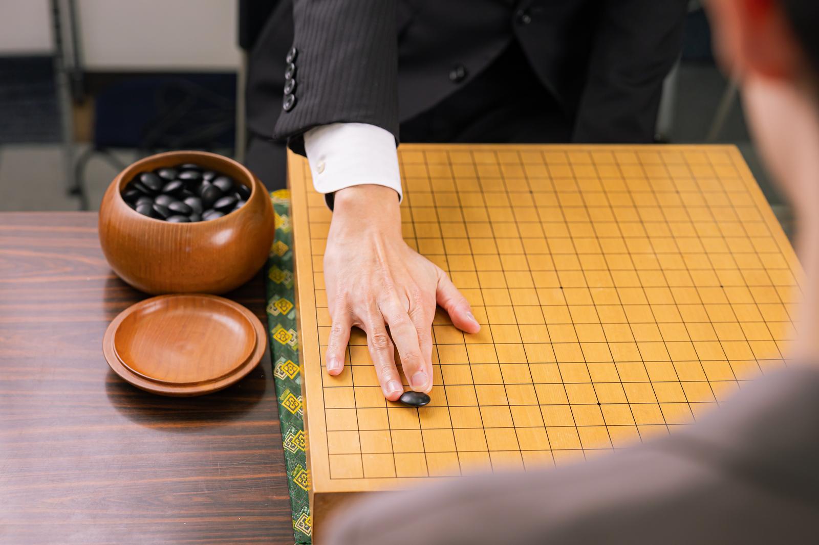 囲碁の対局で黄土色の碁盤に黒い碁石を置こうとする手元