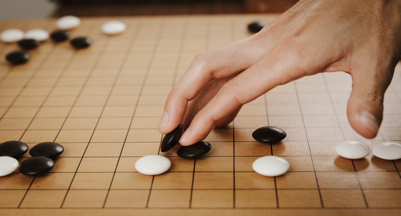 囲碁の碁盤上で黒い碁石を打つプレイヤーの手元のクローズアップ