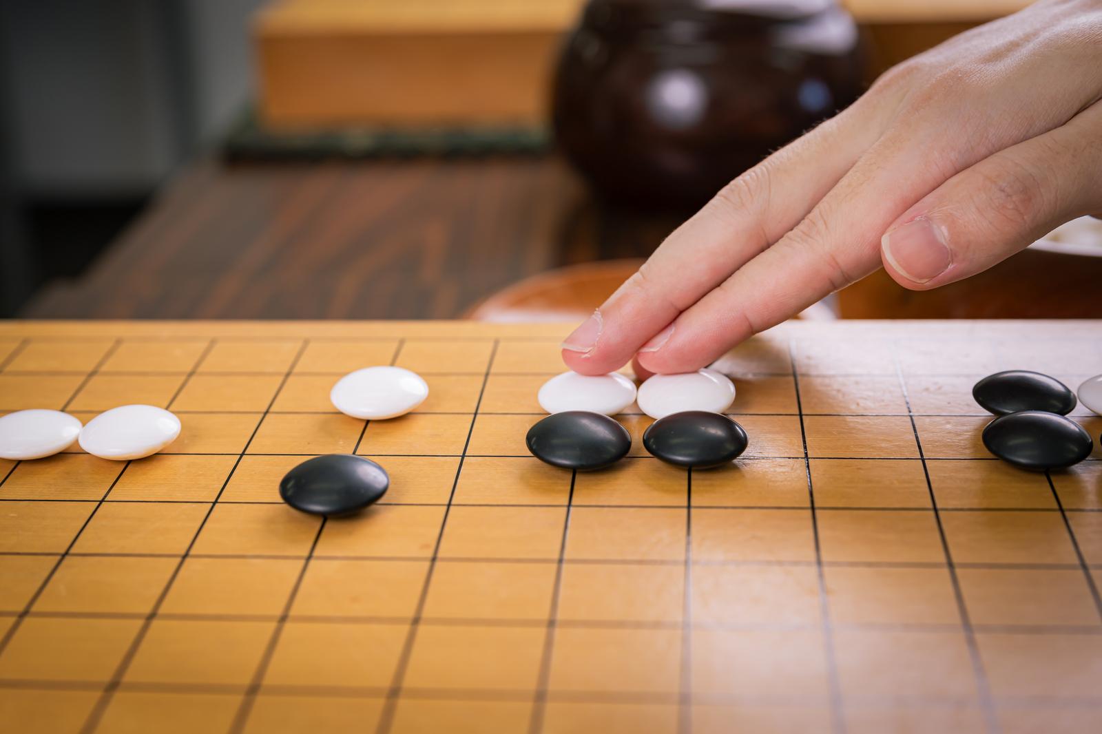 囲碁の対局で白い碁石を碁盤に打つプレイヤーの手元