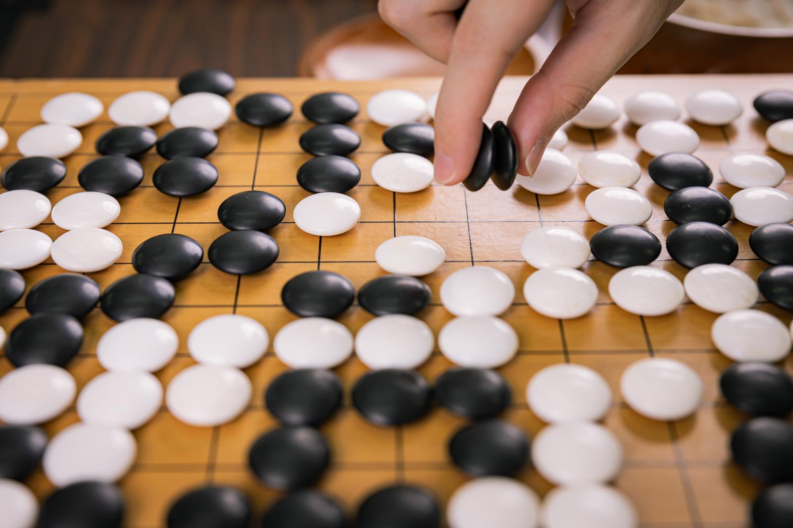 囲碁盤で複数の黒石を手でつまみ上げるプロ棋士の手元
