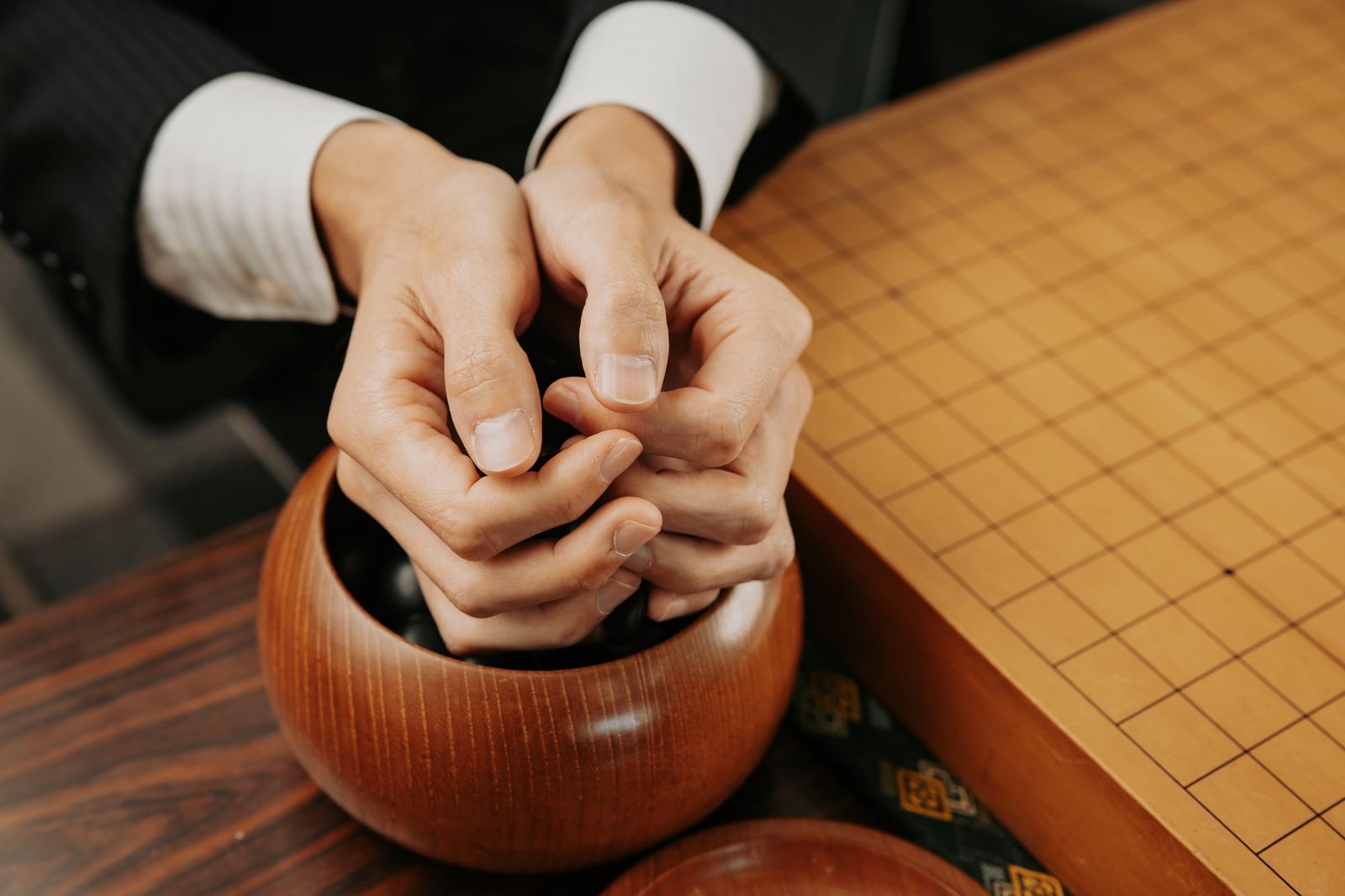 碁笥から碁石を運ぶ両手と碁盤