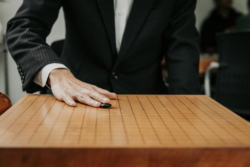 天元を狙う初手、碁石を木製盤面に滑らせて打つ