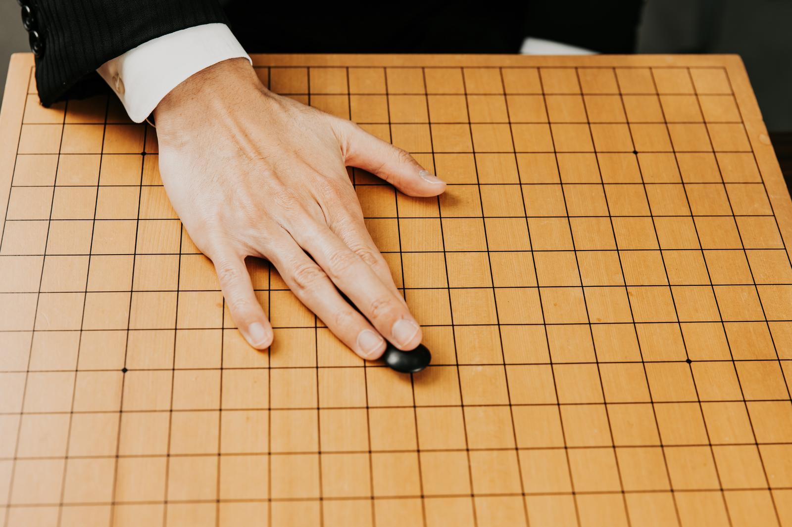 囲碁盤の中央に黒い碁石を置く白襟の手
