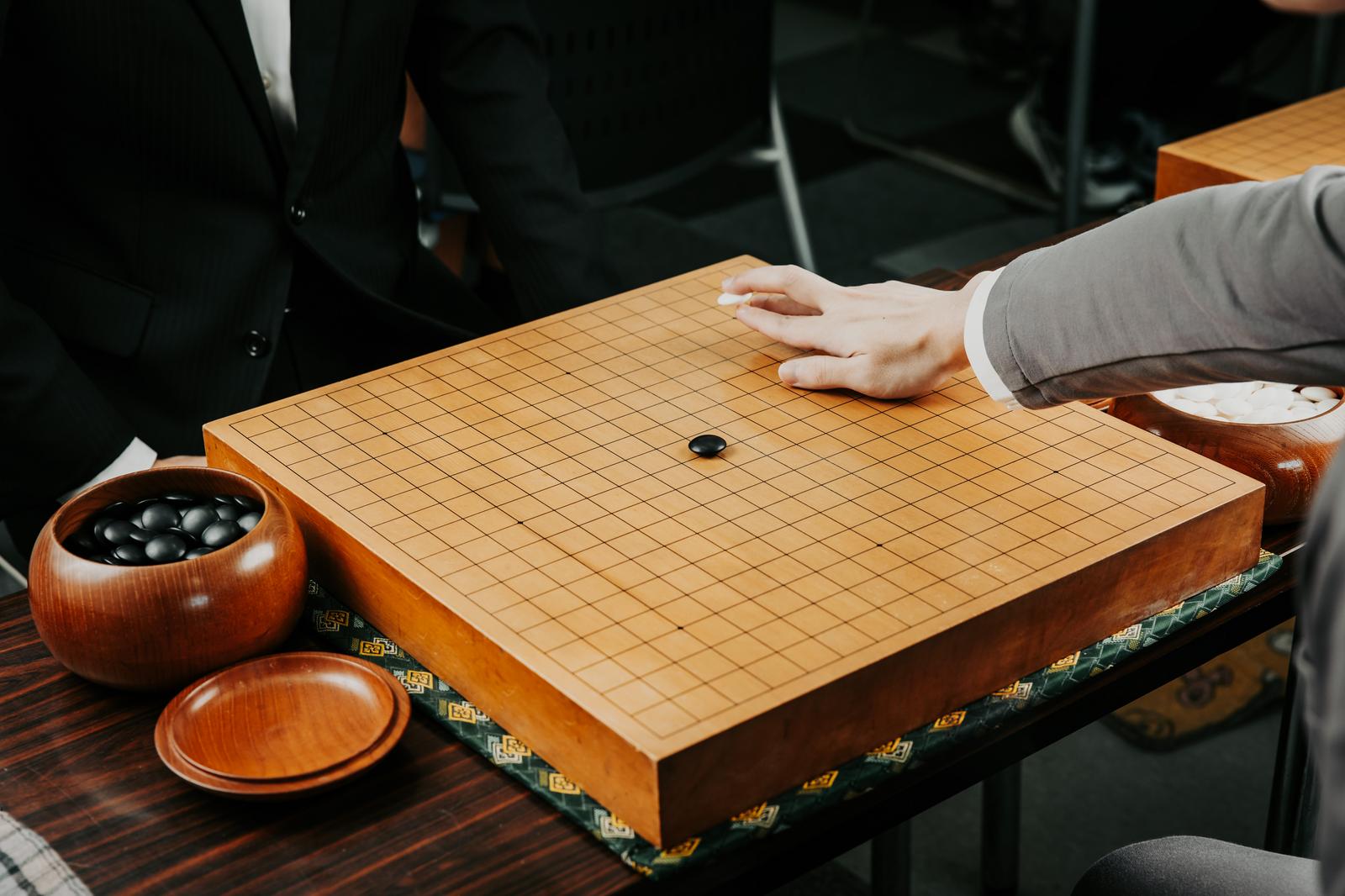 囲碁の碁盤上で白の一手を打つ対局者の手元