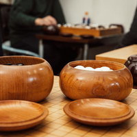 木製の碁笥と碁石が並ぶ囲碁盤の対局風景の写真