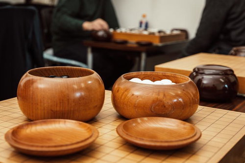 木製の碁笥と碁石が並ぶ囲碁盤の対局風景
